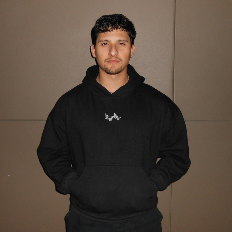 Man wearing a black oversized hoodie with a small embroidered doves logo on chest.